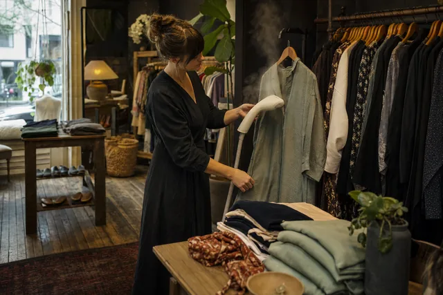 A shop owner steaming a jacket beside the racks in a clothing shop